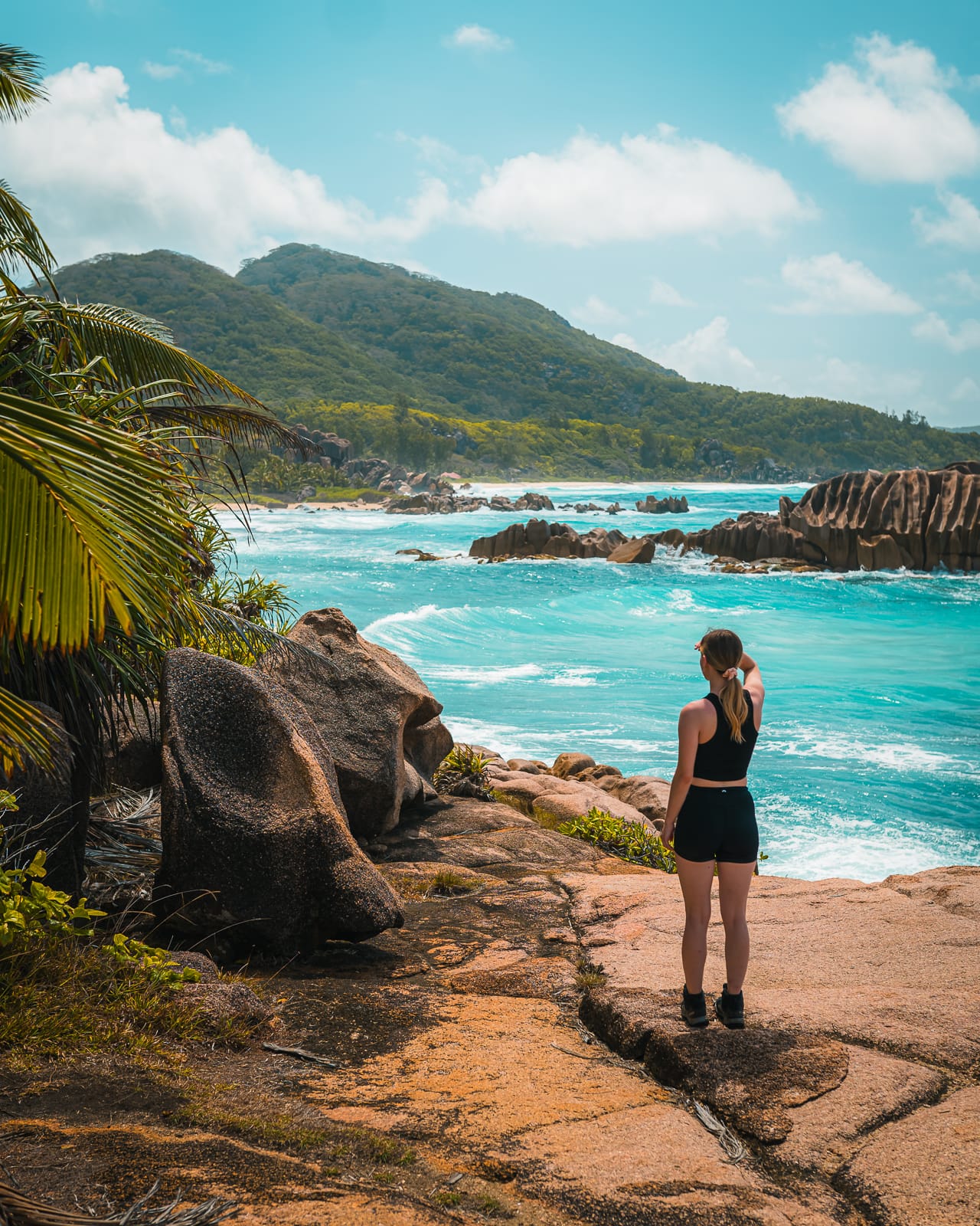 Woman looking out over blue water and mountains on La Digue, Seychelles