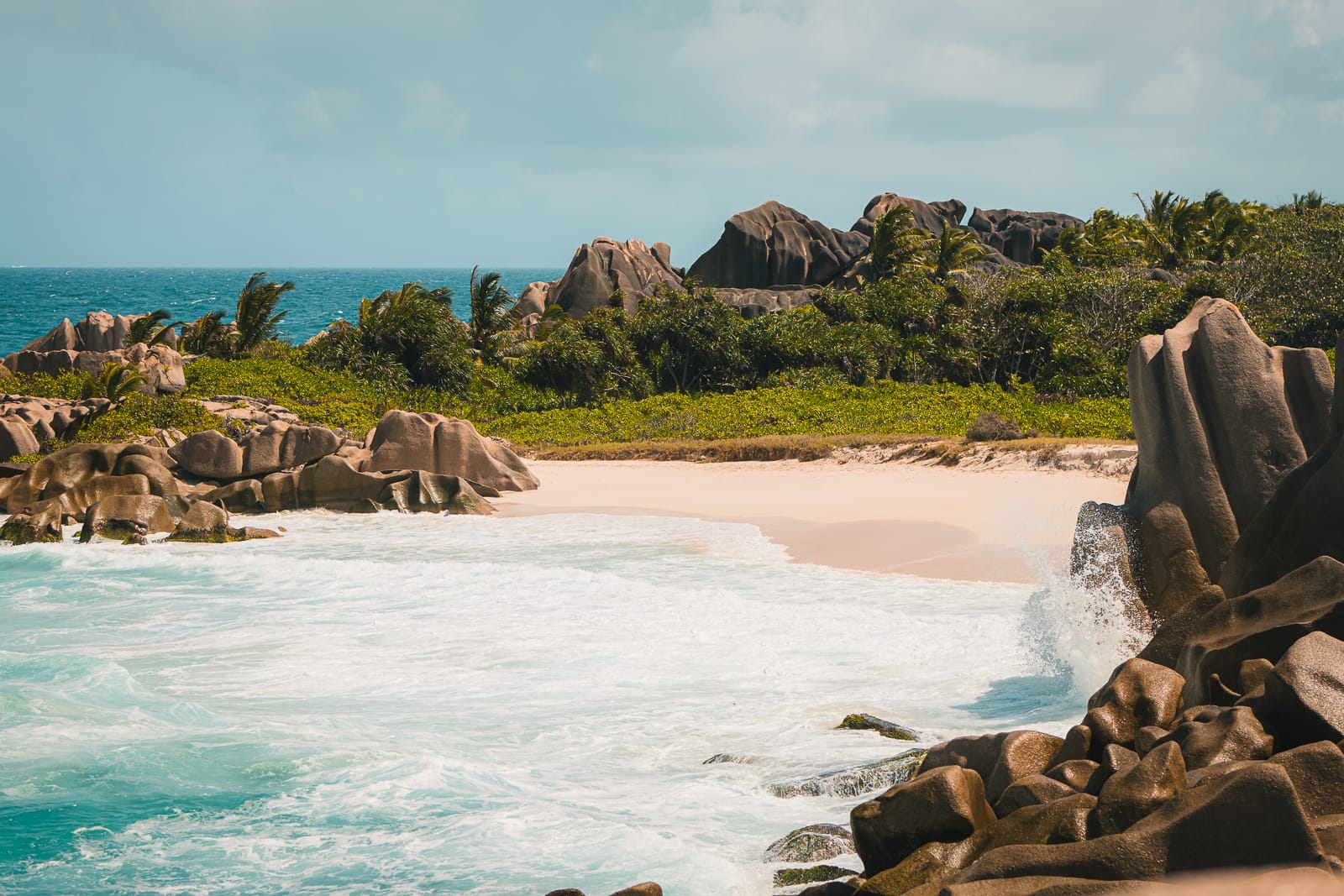 Waves crashing against rocks on a white sand beach in La Digue Seychelles