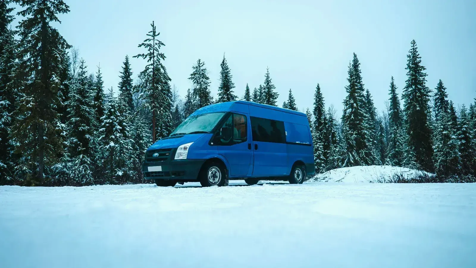 Blue ford transit camper van parked in a snowy forest in Lapland