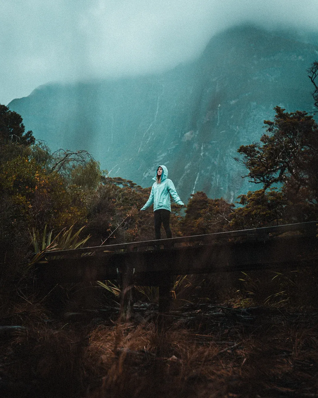 Walker standing on a bridge in rainy conditions at Milford Sound