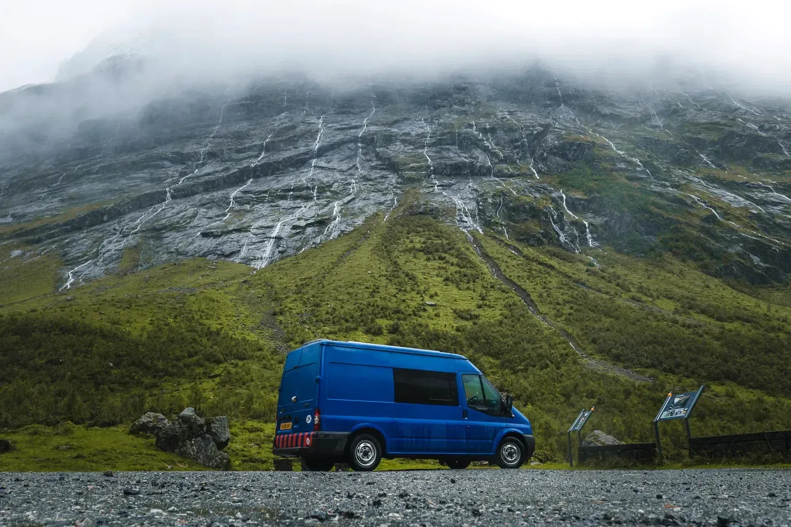 Blue camper van parked in a waterfall valley in Norway