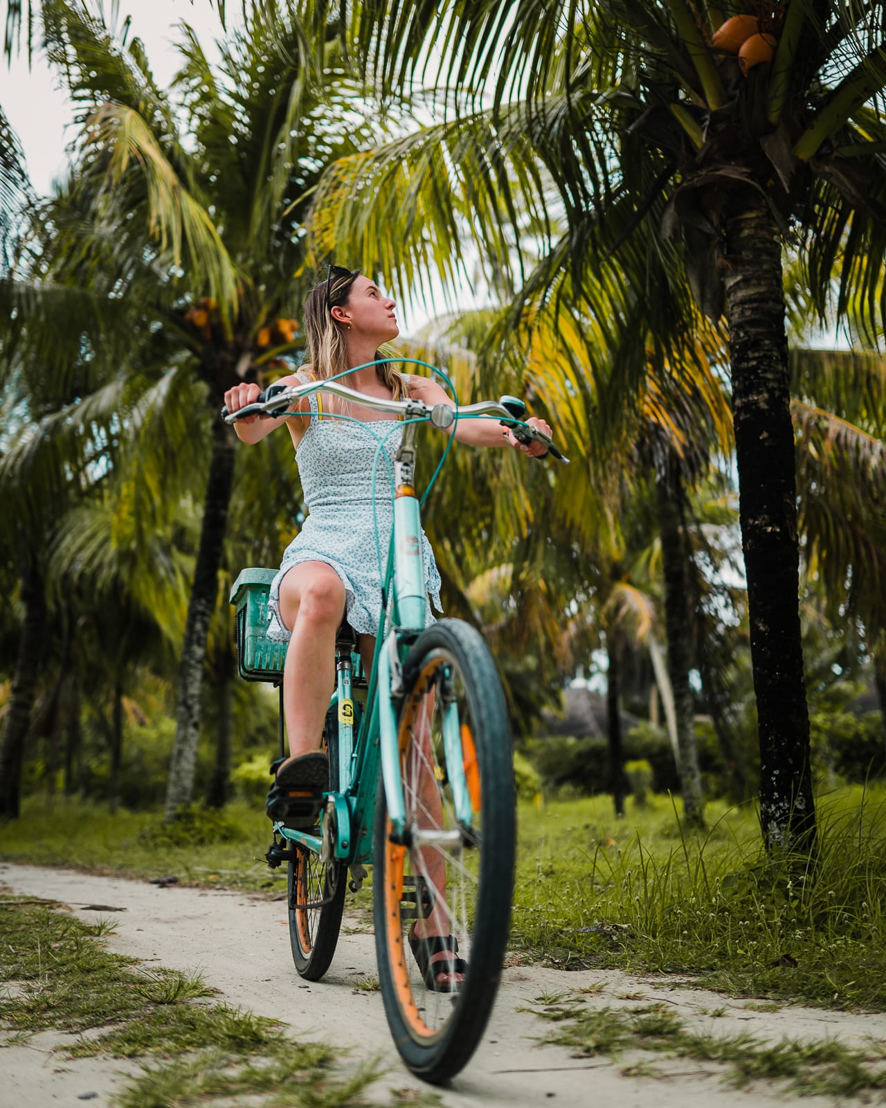 Woman sitting on a bike on a sandy road under palm trees in La Digue