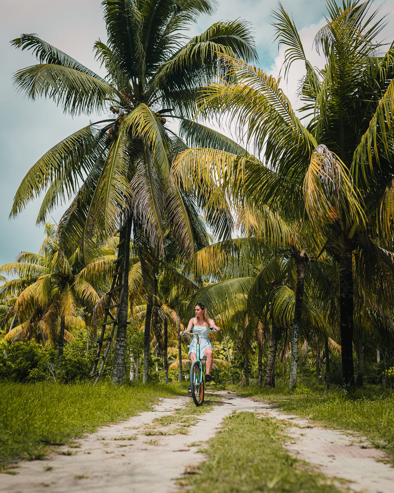 View of a woman riding a bike down a sandy road in Union Estate, La Digue