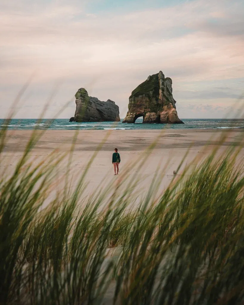 woman walking on wharariki beach with Archway Islands in background