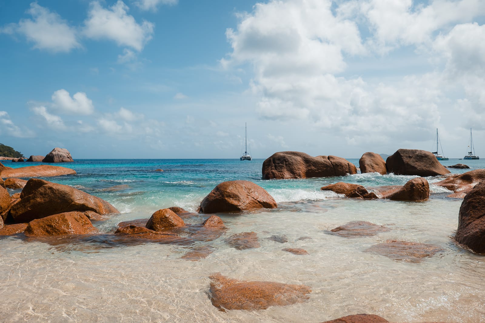 rocks on a beach with clear blue water and boats in the background