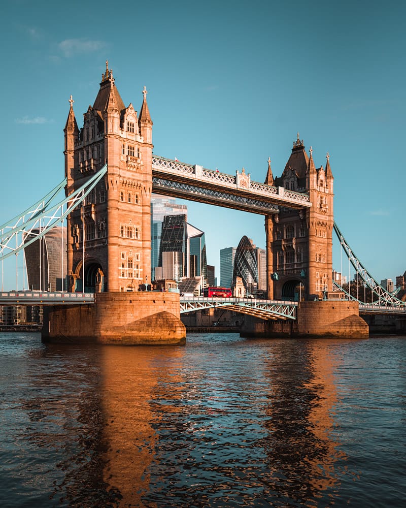 View of London skyline through Tower Bridge with golden light from riverside.