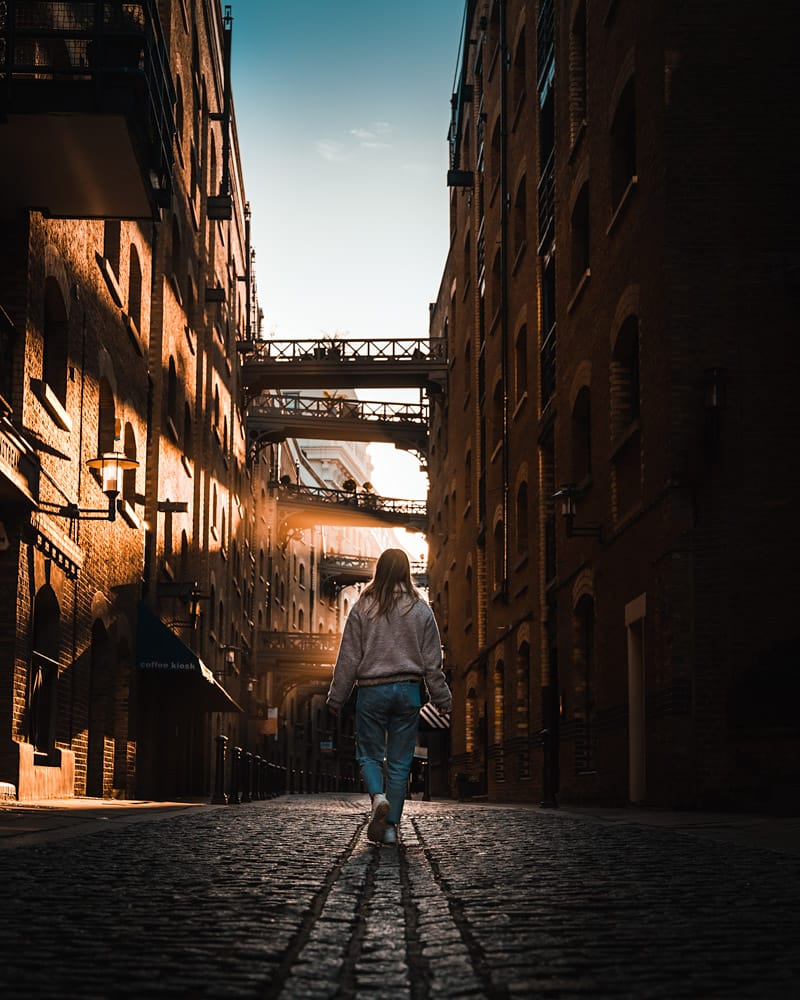 Woman standing under bridges on a cobbled street at sunrise at Shad Thames, London