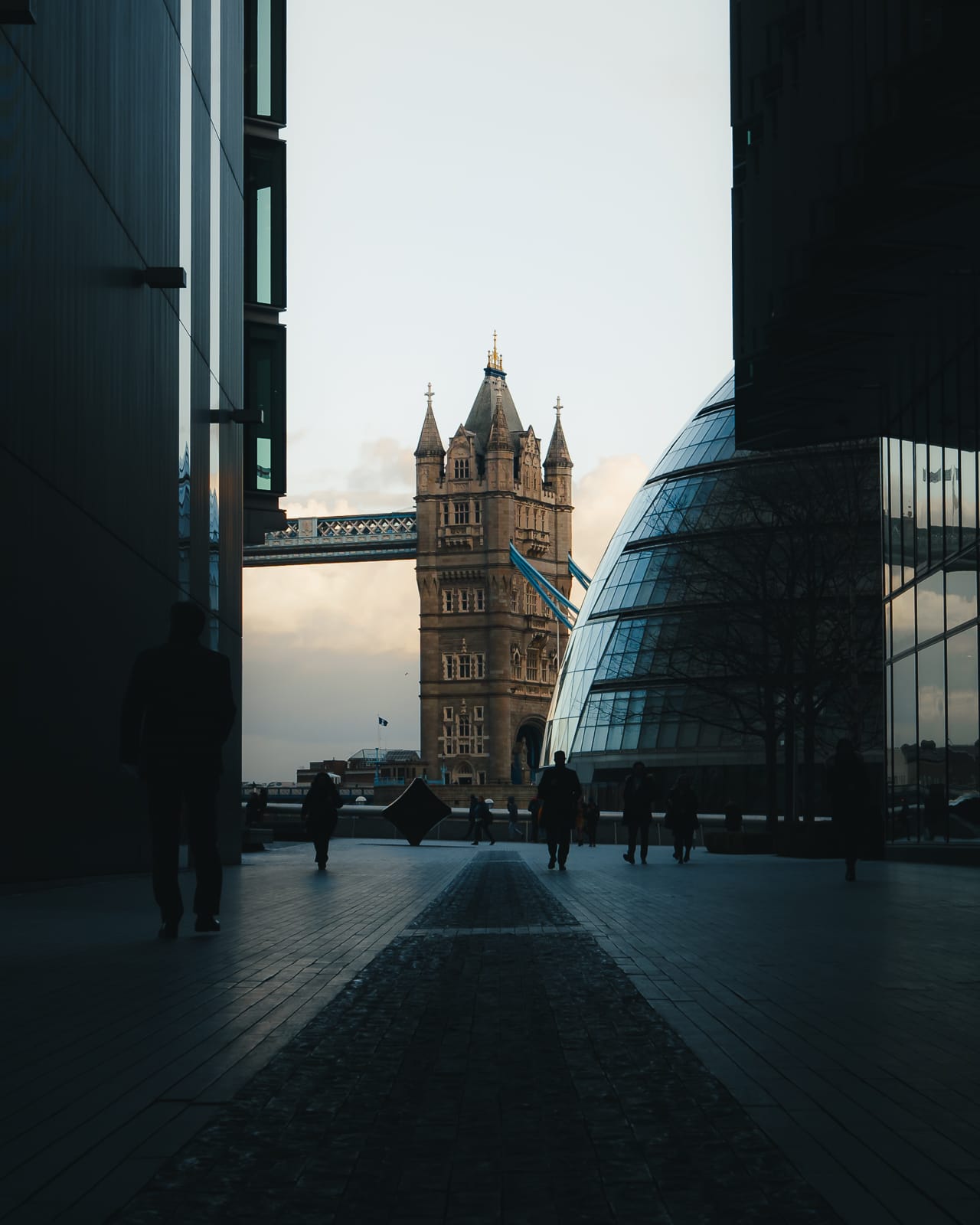 people walking between buildings with tower bridge in the background