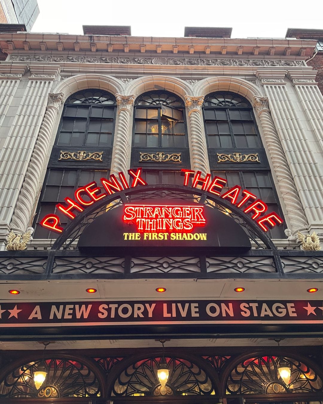 red neon sign of pheonix theatre showing stranger things in london