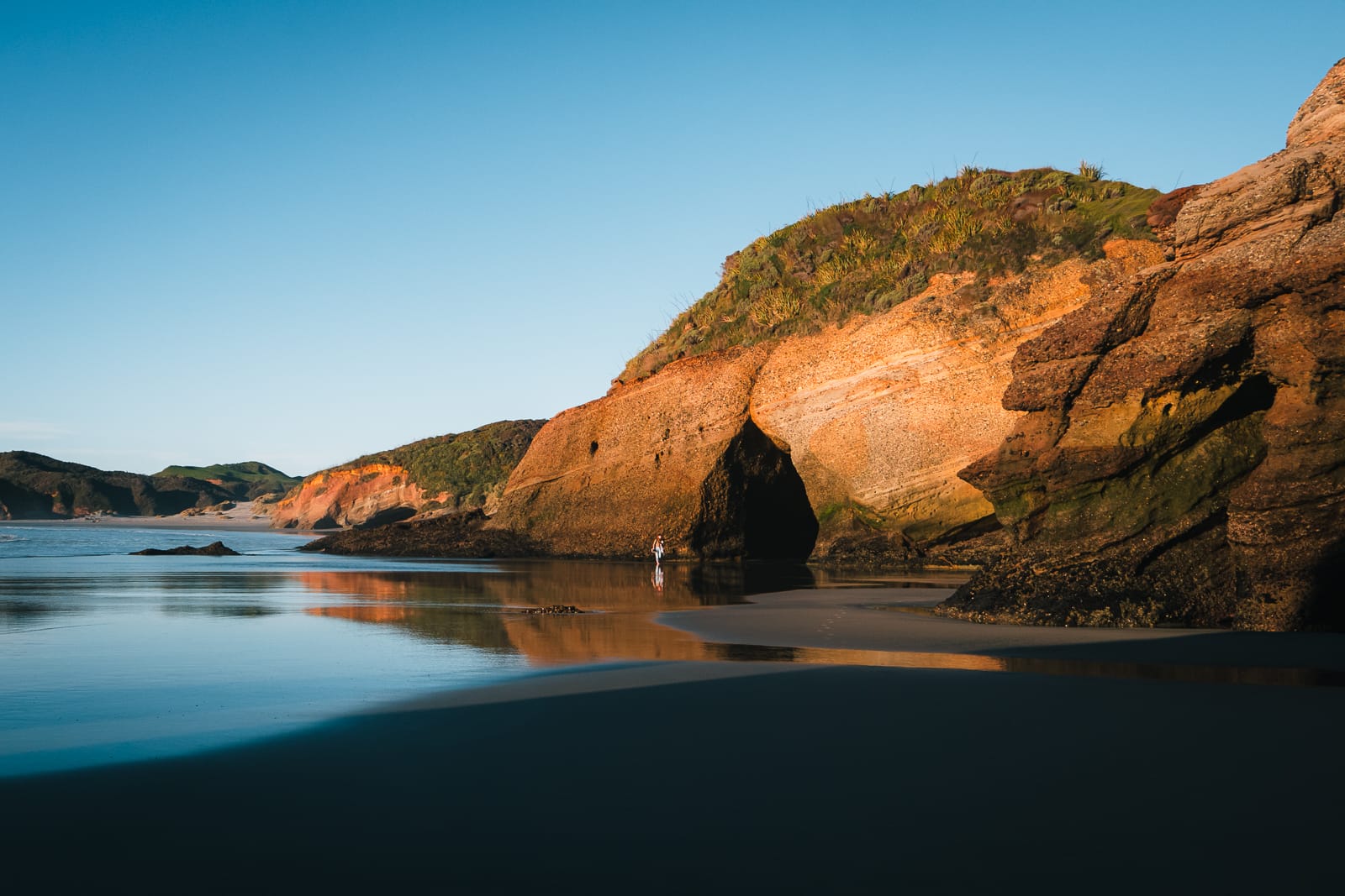 woman walking beside cliff at wharariki beach