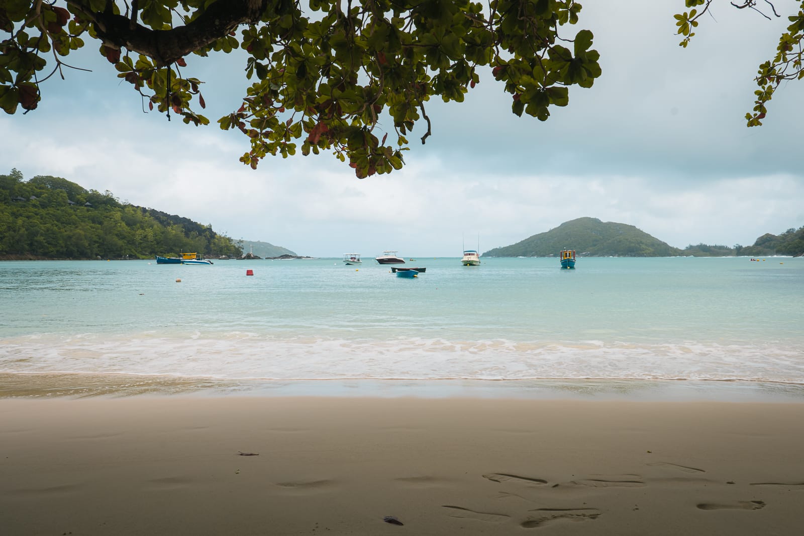 Sandy beach with boats floating on the turqoise water in Mahe, Seychelles 