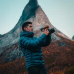 Photographer Rory Watson holding a camera, standing under Stetind mountain in Norway