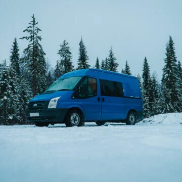 Blue ford transit camper van parked in a snowy forest in Lapland