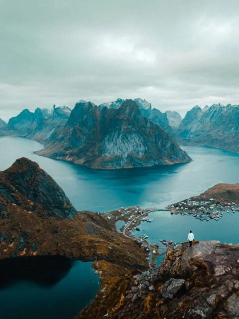 Panoramic aerial view of a hiker stading at the top of Reinebringen Mountain looking over Reine in Lofoten Islands, Norway